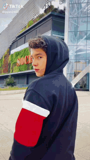 a young man wearing a black hoodie is standing in front of a building that says socce