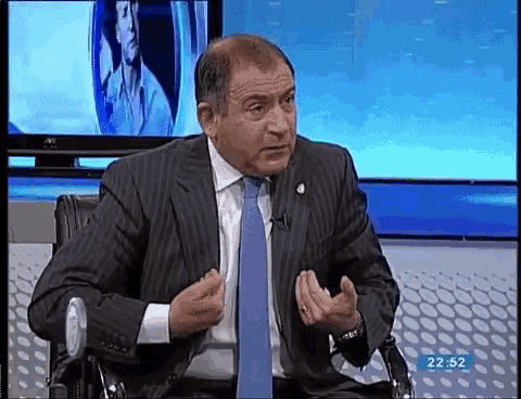a man in a suit and tie is sitting in front of a tv screen with the time 22:52