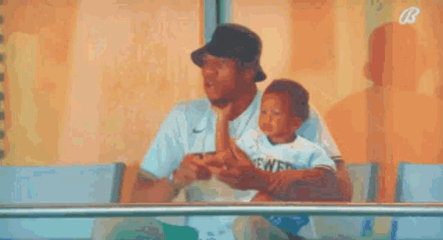 a man is holding a small child in his arms while sitting in a stadium .