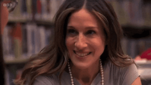 a woman is smiling and wearing a pearl necklace in front of a bbc logo