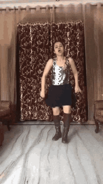 a woman in a skirt and boots is dancing in front of a curtain