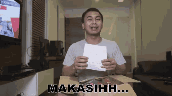 a man is holding a piece of paper in front of a box that says makasih