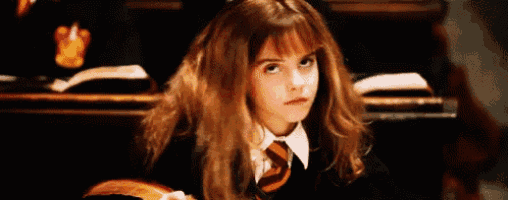 a young girl in a harry potter uniform and tie is sitting in a classroom looking at the camera .
