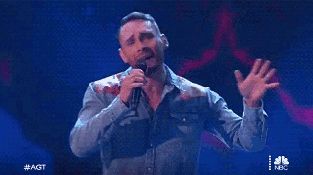a man singing into a microphone on a stage with a nbc logo behind him