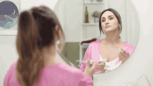 a woman in a pink robe looks at herself in the mirror