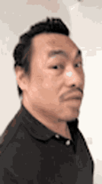a man with a mustache is wearing a black polo shirt and making a funny face .