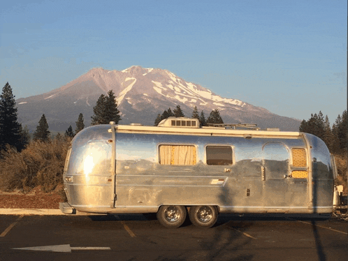 a silver airstream trailer is parked in a parking lot with a mountain in the background