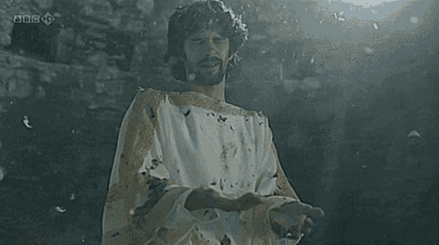 a man in a white and gold robe with a bbc logo on the bottom