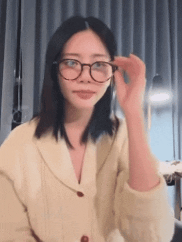 a woman wearing glasses and a sweater is adjusting her glasses .