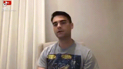 a man in a t-shirt is sitting in a chair in front of a white wall .