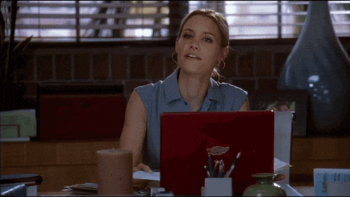 a woman sits at a desk with a red laptop that says ' macbook pro ' on the back