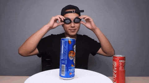 a man wearing goggles stands next to a can of pepsi and a can of coca-cola