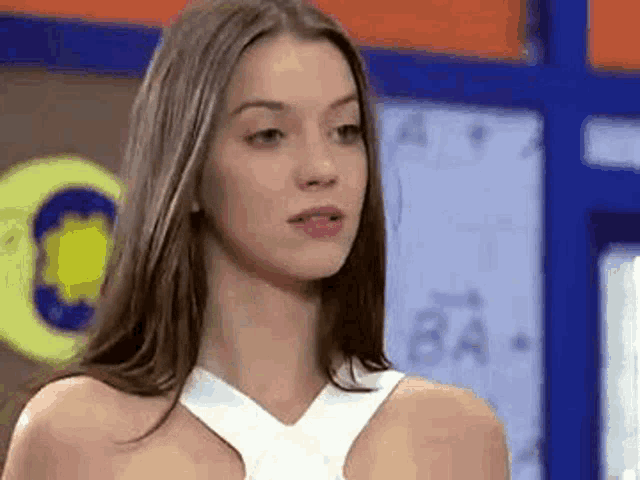 a woman in a white dress is standing in front of a blue wall and looking at the camera .