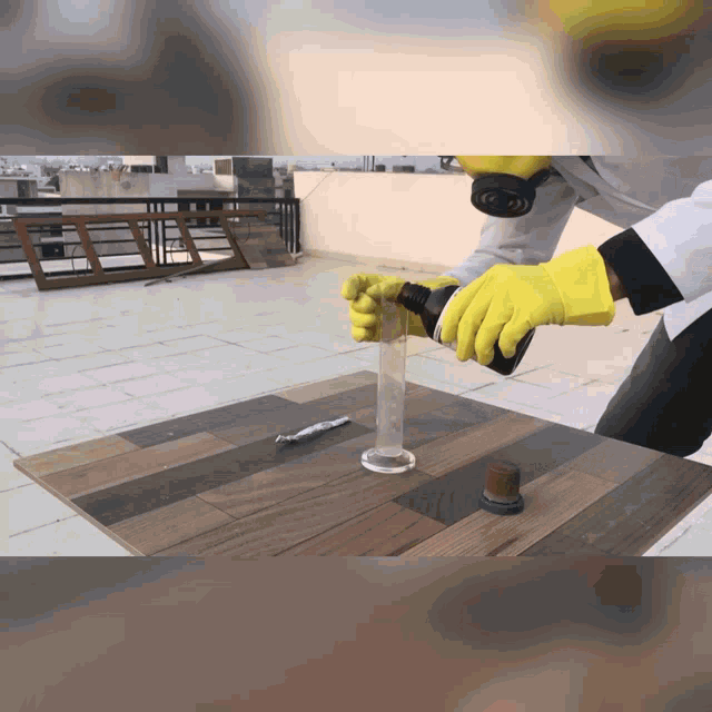 a person wearing yellow gloves is pouring liquid into a glass beaker