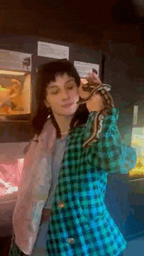 a woman in a plaid jacket is holding a snake over her head .