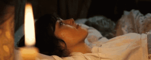 a woman is laying in a bed with a candle lit next to her .