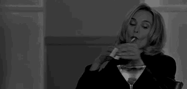 a woman is smoking a cigarette while holding a martini glass .