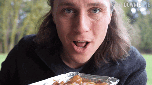 a man with long hair is eating french fries and the words downie live are above him