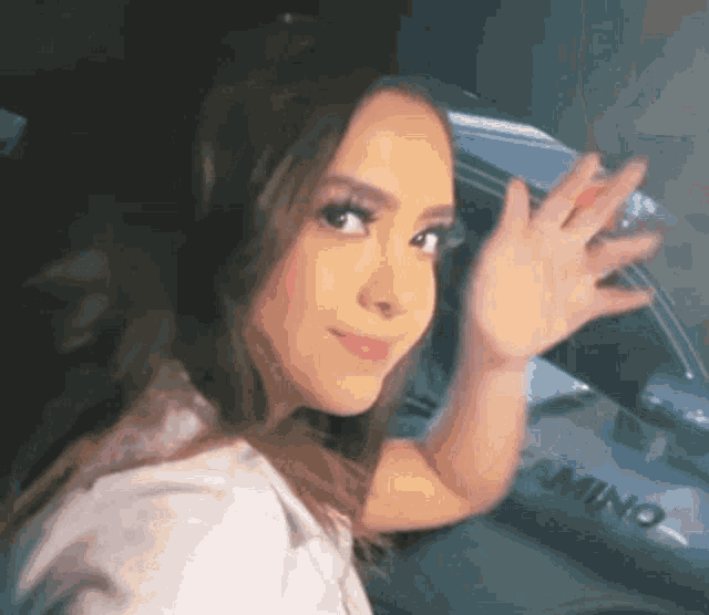 a woman is standing in front of a car and waving at the camera .