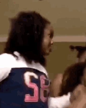 a woman wearing a blue and white jersey with the number 58 on it is standing in a room with other people .