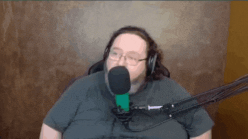 a man wearing glasses and headphones is sitting in front of a green microphone