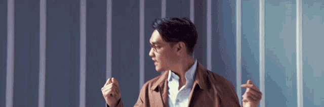 a man in a brown jacket and white shirt is standing in front of a blue and white striped wall .