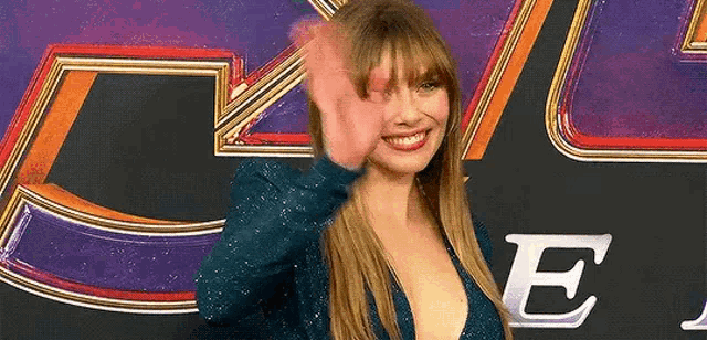 a woman in a blue dress is standing on a red carpet and waving at the camera .