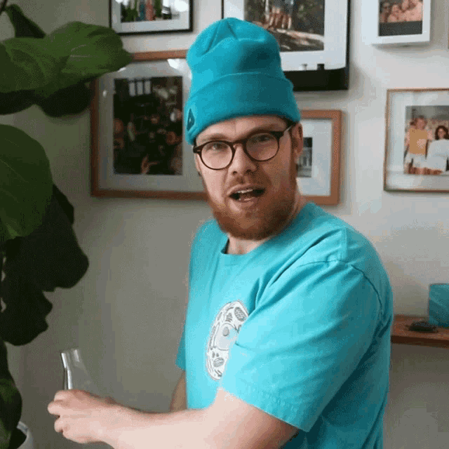 a man wearing a blue beanie and glasses is standing in front of a wall with pictures on it