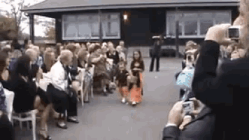 a man is taking a picture of a girl walking down the aisle at a wedding .