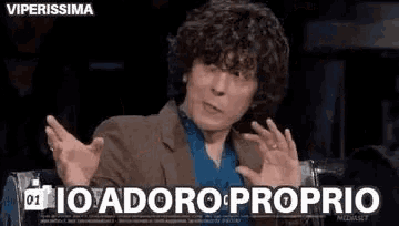 a man with curly hair is making a funny face while sitting in a chair with his hands outstretched .