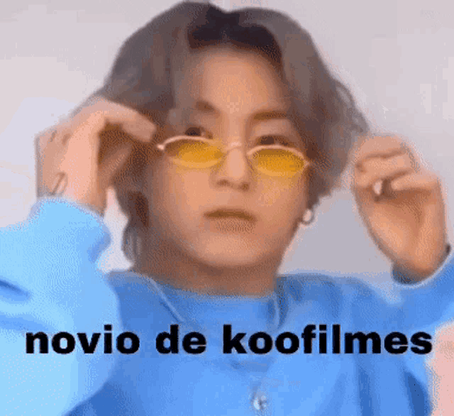 a young man wearing sunglasses and a blue sweater with the words novio de koofilms written on it .
