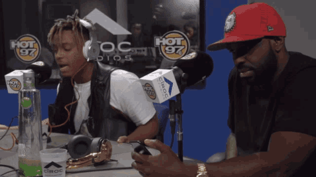 a man in a red hat talks into a microphone in front of a hot 97 sign