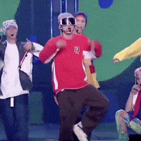 a group of people are dancing on a stage and one of them is wearing a red shirt with the letter e on it