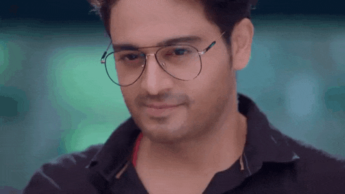 a man wearing glasses and a black shirt is smiling and looking down .