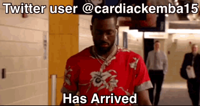 a man in a red shirt is walking down a hallway with the words twitter user @cardiackemba15 has arrived above him
