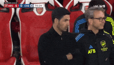 a man wearing a jacket that says afs on it stands in a soccer stadium