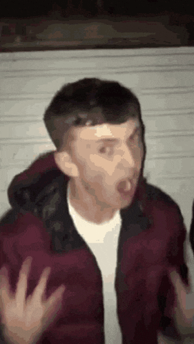 a man in a red jacket is making a funny face while standing in front of a wall .