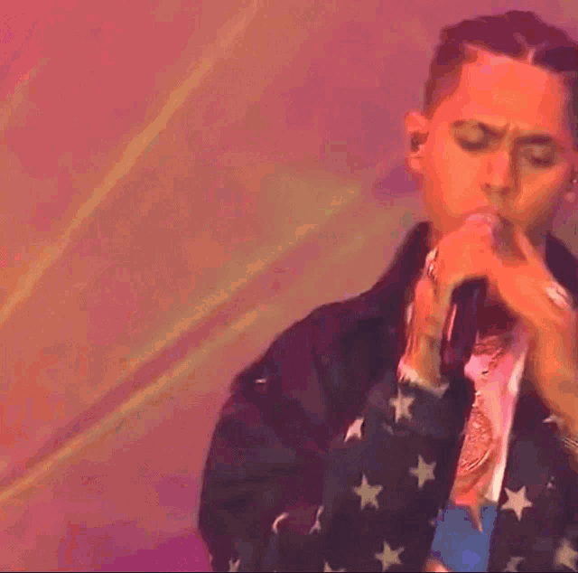 a man is singing into a microphone while wearing an american flag jacket