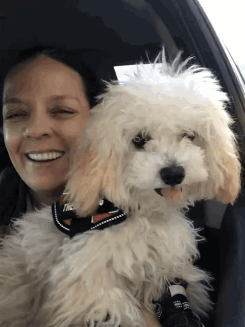 a woman is smiling while holding a small white poodle