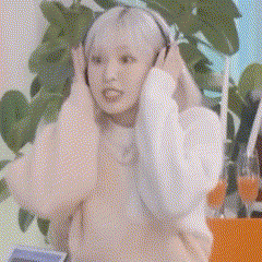 a woman with white hair is wearing headphones and covering her ears while sitting in front of a plant .