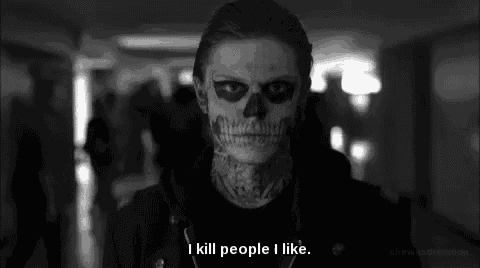 a man with a skull painted on his face is standing in a hallway with a quote .