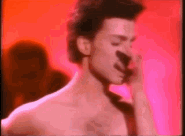 a shirtless man is singing into a microphone in front of a red background .