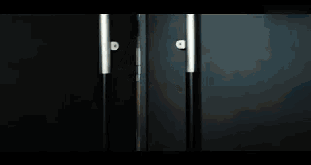 a woman in a white suit is standing in a dark room looking out a window .