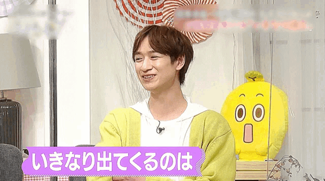 a man in a yellow cardigan is sitting in front of a yellow stuffed animal with a cartoon face on it