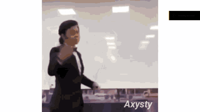 a woman in a suit and tie is standing in front of a whiteboard in a room .