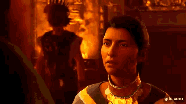 a woman wearing a gold necklace is standing in a dark room with a man standing in the background .