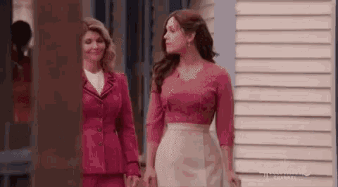 two women in pink dresses are standing next to each other in front of a building .
