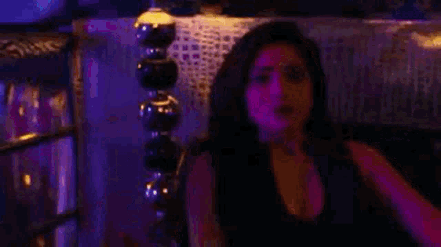 a woman is sitting in a dark room with purple lights and talking to someone .