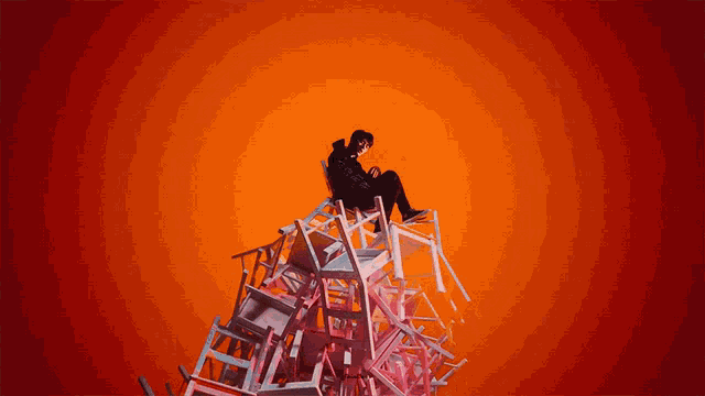 a person sitting on top of a pile of chairs with a red background