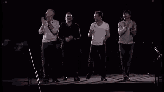 a group of men are standing on a stage in front of microphones and clapping .